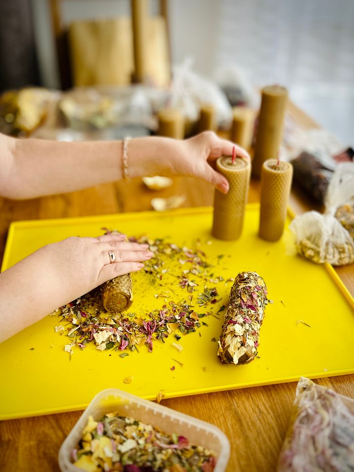 our-experience Close-up of hands crafting floral scented candles on a yellow tray.