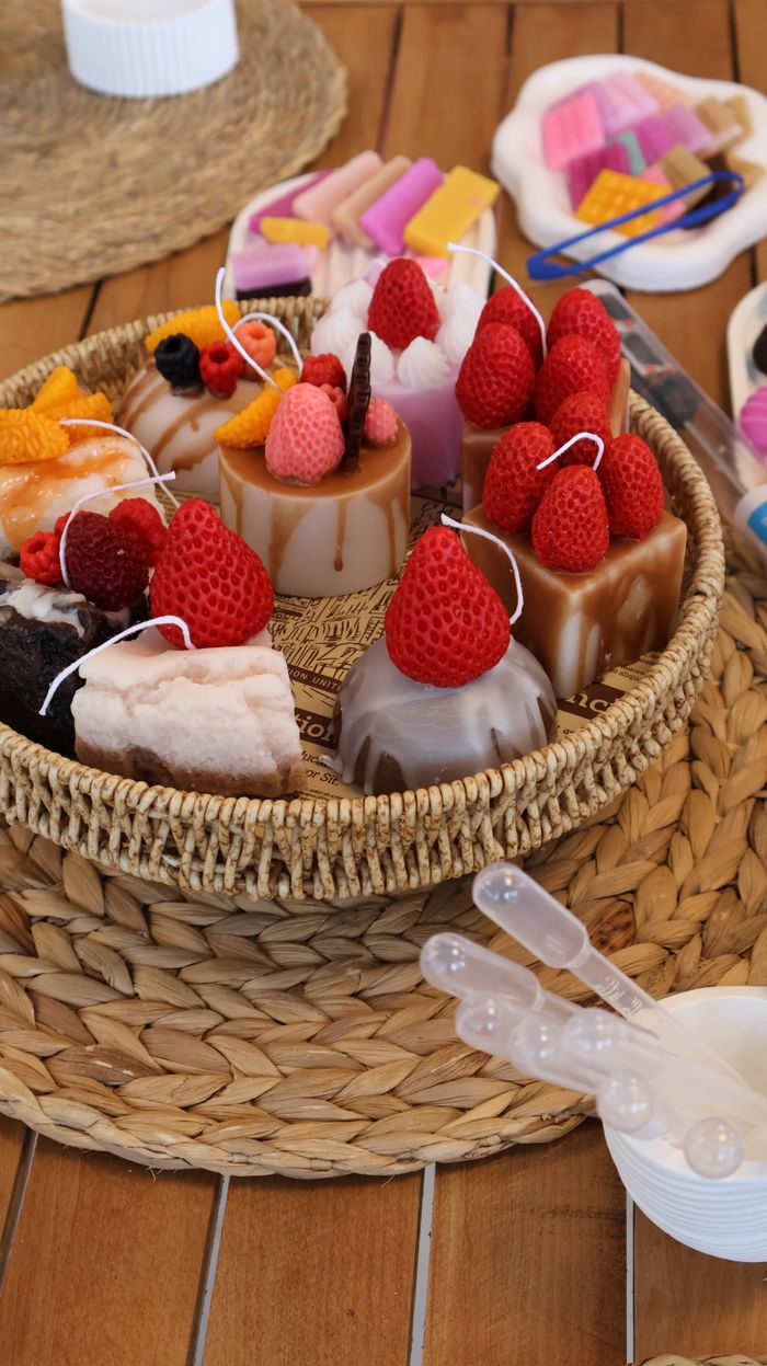 gallery-2 A vibrant display of candles shaped like desserts, artistically arranged in a woven basket.