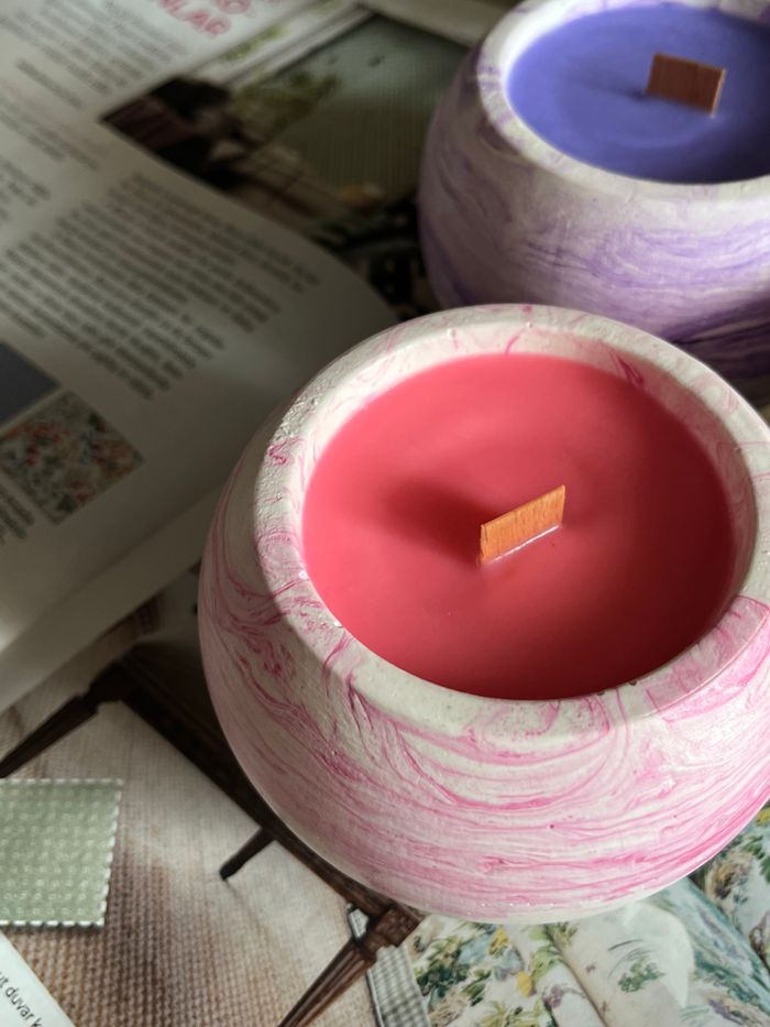 why-choose-us Pink and purple candles with wooden wicks on a table, featuring open magazines.