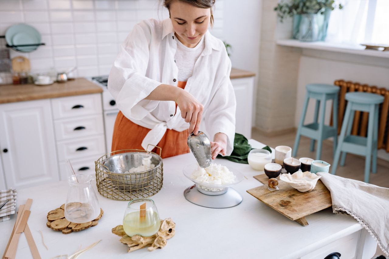 hero-img-01 Woman crafting candles at home with natural wax in a bright kitchen setting.